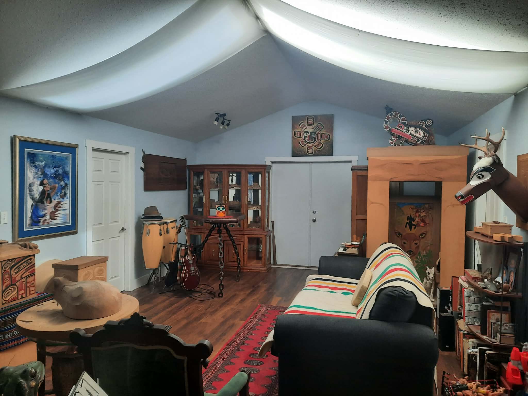 Looking across the studio: a sun mask above the doorway, a carved deer head, drums and a guitar at rest.